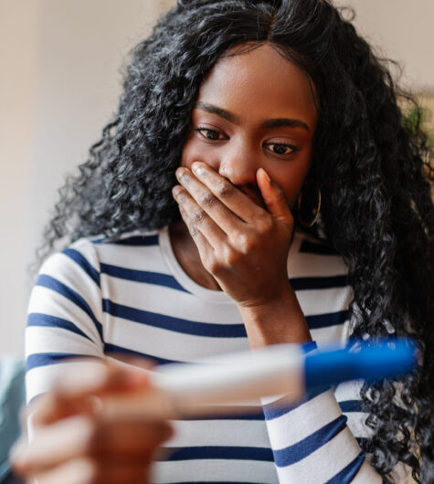 Shocked young woman holding positive pregnancy test. Unwanted pregnancy concept.