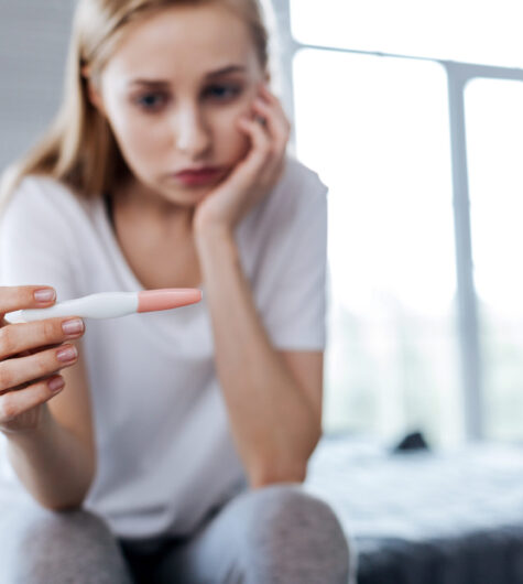 young woman holding a pregnancy test and looking worried.