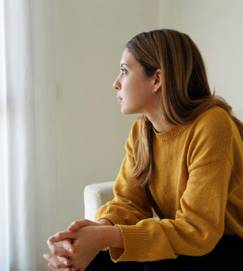 Melancholic sad woman looking through the window at home