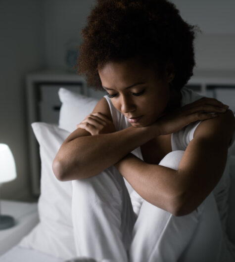 Sad African American woman sitting in her bed late at night, she is pensive and suffering from insomnia.